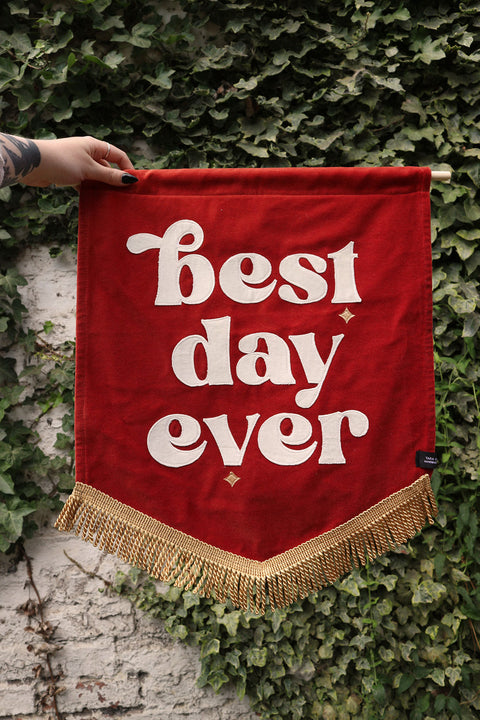 Terracotta wedding sign with white "best day ever" applique text on a velvet background adorned with ivy leaves.