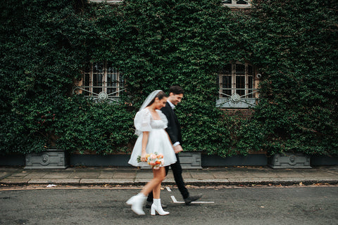 Bride and groom walking outdoors against a backdrop of lush green ivy.