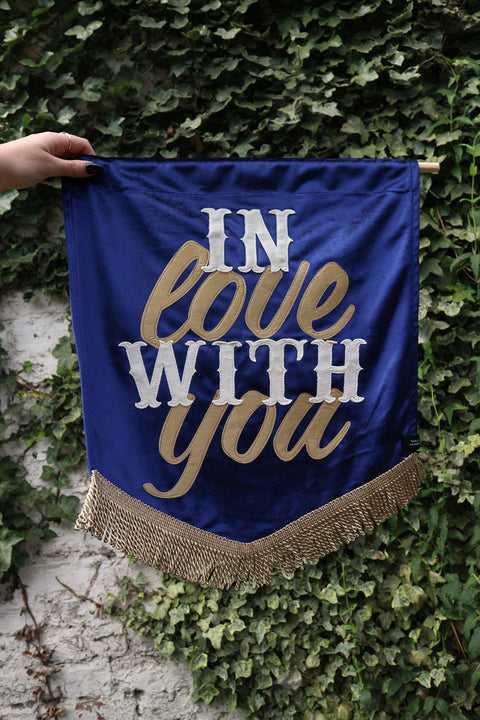 A vibrant dark blue wedding banner featuring "in love with you" in velvet, set against a lush ivy background.