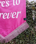 Close up of velvet banner in pink with light pink fringing and gold star applique on ivy leaf background.