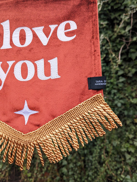 Close up of velvet banner with gold fringing and white star applique on ivy leaf background.