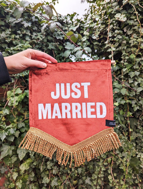 Velvet banner in terracotta with "just married" text on ivy leaf background.