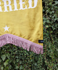 Close up of velvet wedding banner in yellow white text, pink fringing and star applique on ivy leaf background.