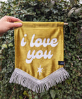 Velvet wedding banner in gold with "i love you" text on ivy leaf background.