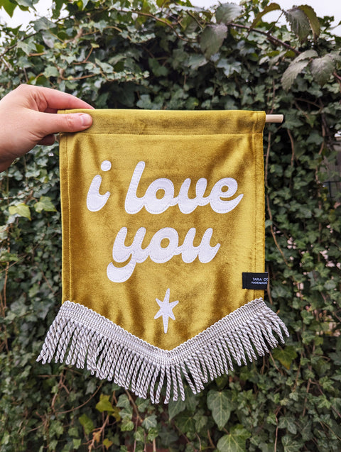 Velvet wedding banner in gold with "i love you" text on ivy leaf background.