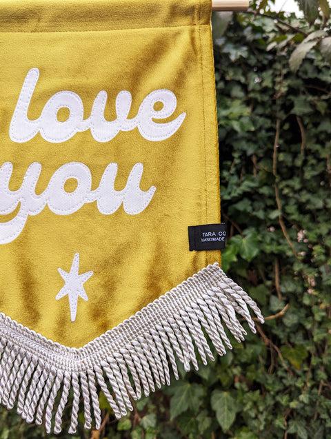 Velvet wedding banner in gold with "i love you" text, white fringing and white star applique on ivy leaf background.
