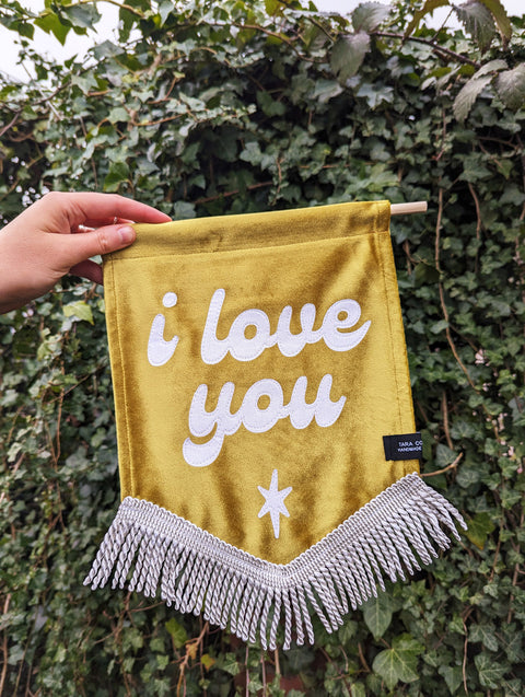 Velvet wedding banner in gold with "i love you" text on ivy leaf background.