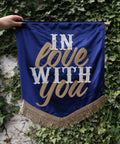 A vibrant dark blue wedding banner featuring "in love with you" in velvet, set against a lush ivy background.