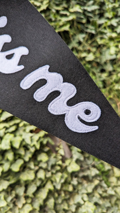 Felt pennant banner in black and white with "kiss me" text with white stitching on ivy leaf background.