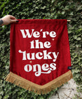 Red wedding banner saying "we're the lucky ones" on ivy backdrop.