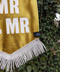 Velvet wedding banner in gold with "mr and mr" white text and white fringing detail on ivy leaf background.