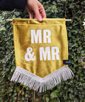 Velvet wedding banner in gold with "mr and mr" white text and white fringing on ivy leaf background.