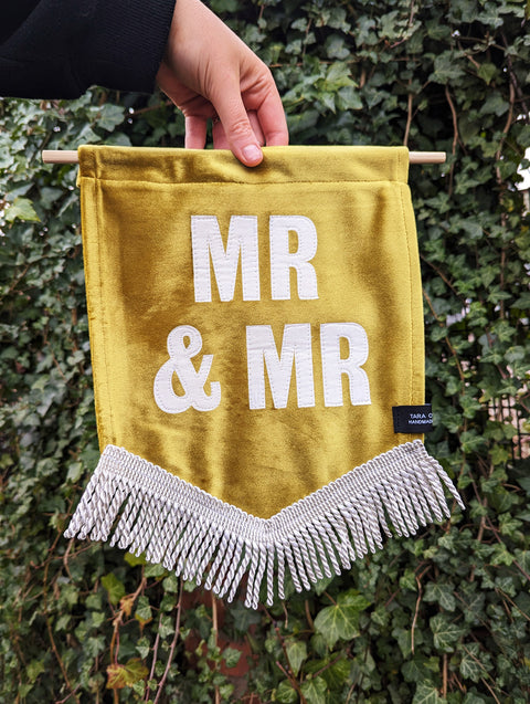 Velvet wedding banner in gold with "mr and mr" white text and white fringing on ivy leaf background.