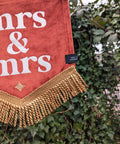 Velvet mini banner in terracotta with "mrs & mrs" text, gold fringing and gold star applique on ivy leaf background.