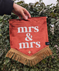 Velvet mini banner in terracotta with "mrs & mrs" text and gold fringing on ivy leaf background.