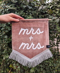 Velvet wedding banner in pink with "mrs and mrs" white text and white fringing on ivy leaf background.