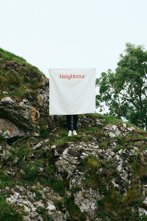 Square cotton banner in white with "neighbour" text in red across the top