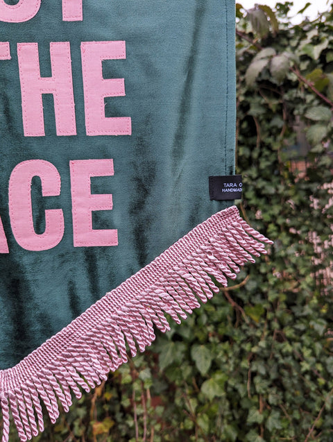 Velvet wedding banner in green with "this must be the place" pink text and pink fringing on ivy leaf background.