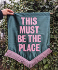 Velvet wedding banner in green with "this must be the place" pink text and pink fringing on ivy leaf background.