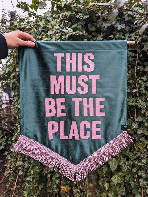 Velvet wedding banner in green with "this must be the place" pink text and pink fringing on ivy leaf background.