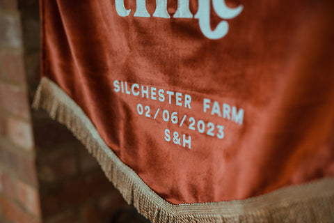 Close up of velvet wedding banner in terracotta with "venue details" text, showing gold fringing.