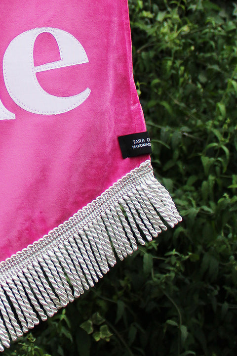Close up of velvet wedding banner in pink with "you and me" white text and silver fringing