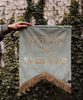 Velvet wedding banner in sage green with "always and forever" gold text and gold fringing on ivy background