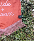 Velvet banner in terracotta with "bride and groom" pink text, and pink fringing on ivy leaf background.
