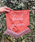 Velvet banner in terracotta with "bride and groom" pink text on ivy leaf background.