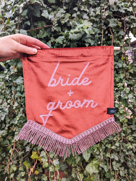 Velvet banner in terracotta with "bride and groom" pink text on ivy leaf background.