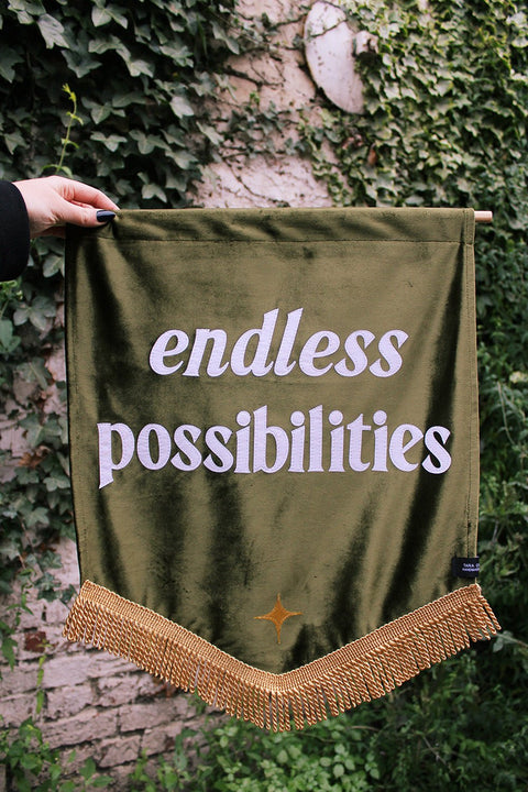 Velvet wedding banner in green with "endless possibilities" white text, gold fringing and gold applique star on ivy background.