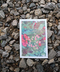 A vibrant A5 risograph print of pomponette flowers rests on a stony floor.