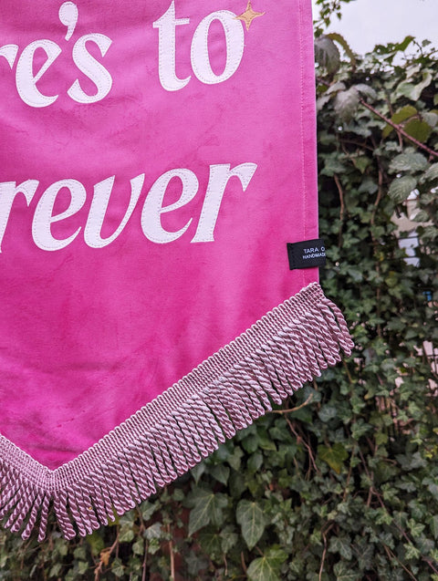 Close up of velvet banner in pink with light pink fringing and gold star applique on ivy leaf background.