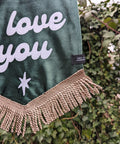 Ivy leaf backdrop with close up of green velvet banner, ivory gold fringing, and "i love you" text.