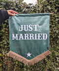 Velvet wedding banner in green with "just married" text and gold fringing on ivy leaf background.