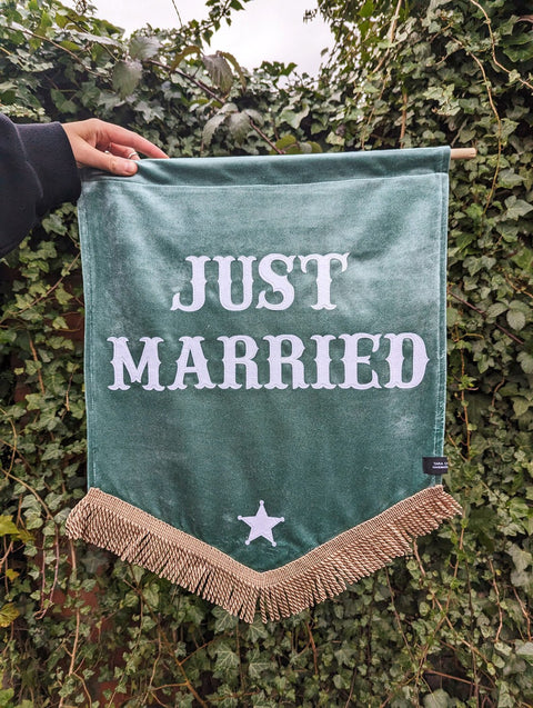 Velvet wedding banner in green with "just married" text and gold fringing on ivy leaf background.