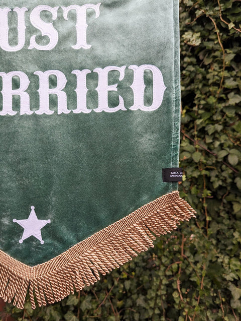 Velvet wedding banner in green with "just married" text, gold fringing and star applique, on ivy leaf background.