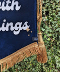 Velvet wedding banner in navy with gold fringing and gold hanging tassel details on ivy leaf background.