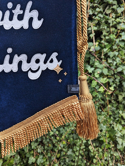 Velvet wedding banner in navy with gold fringing and gold hanging tassel details on ivy leaf background.