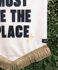 Velvet wedding banner in white with "this must be the place" text, gold fringing and star applique, on ivy leaf background.