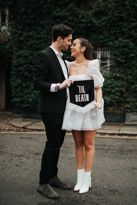 Velvet wedding mini banner in black with "til death" text and white fringing held by married couple.