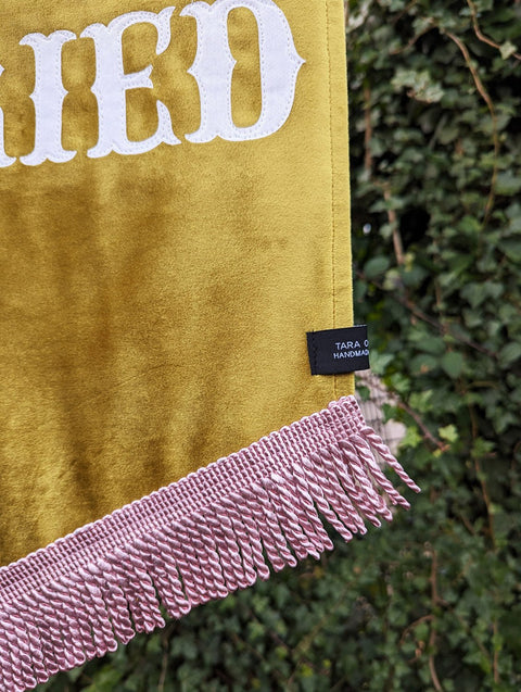 Super close up of velvet wedding banner in yellow showing pink fringing and stitching detail.