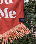 Velvet wedding banner in terracotta with "You and Me" text and peach fringing on ivy leaf background.