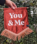 Velvet wedding banner in terracotta with "You and Me" text and peach fringing on ivy leaf background.